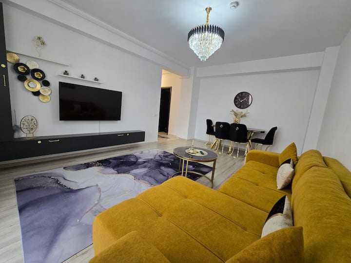 Dhomë ndenje e gjerë dhe e ndritshme, me mobilim modern, ideale për relaksim. Ka një divan të rehatshëm, një Smart TV të madh dhe një zonë elegante ngrënieje.