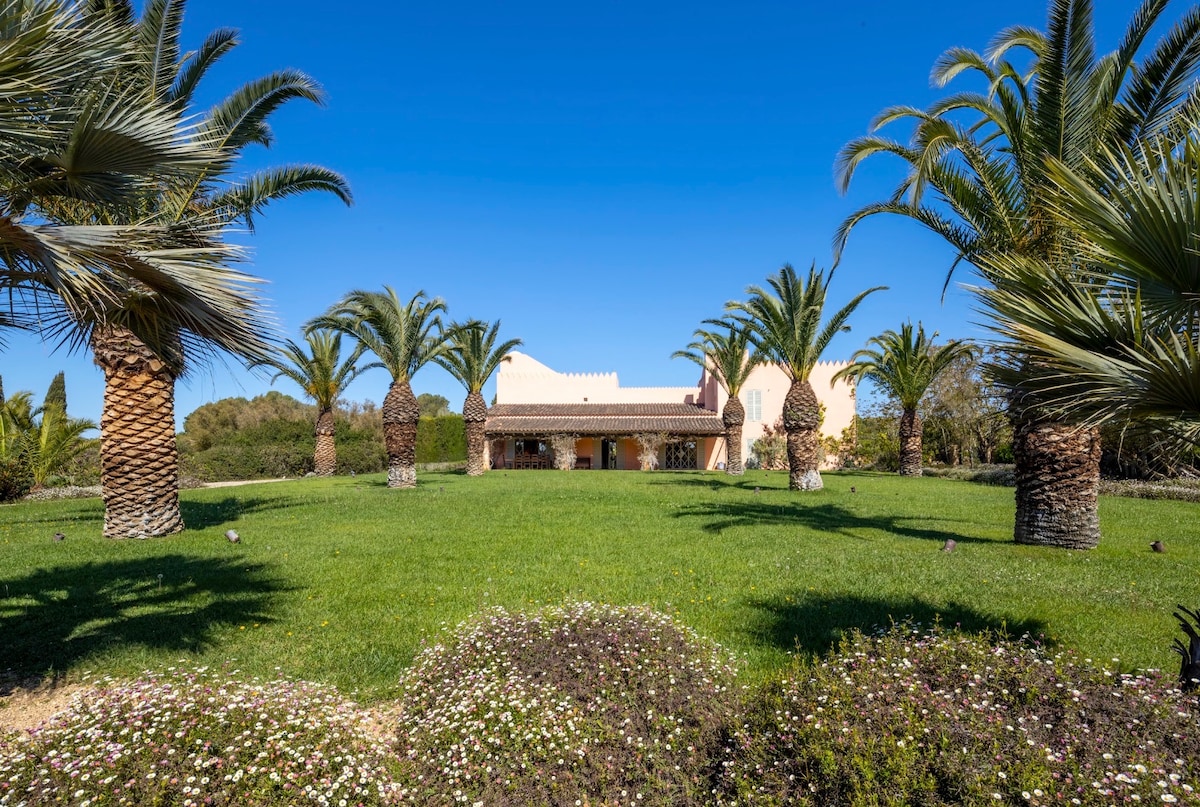 Front of The Arabic House, peach walls and a tiled porch across the lawn