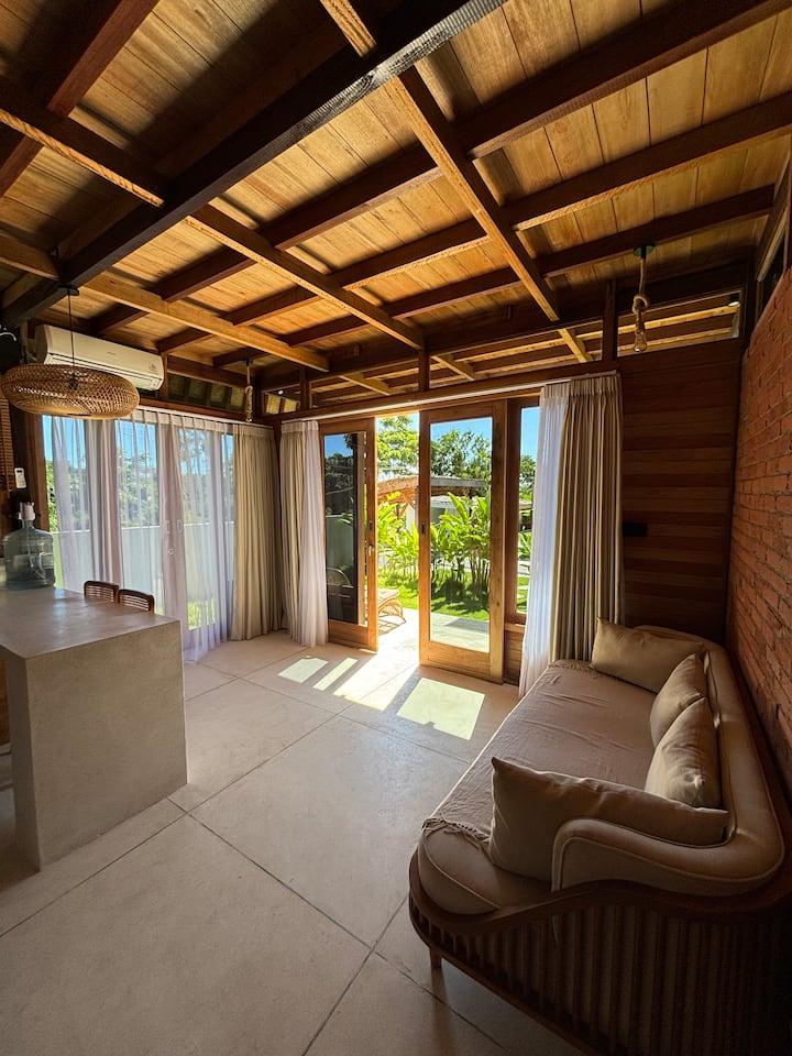 Espace de vie lumineux et confortable au design en bois naturel, donnant directement sur un jardin paisible, parfait pour se détendre dans une atmosphère tropicale.