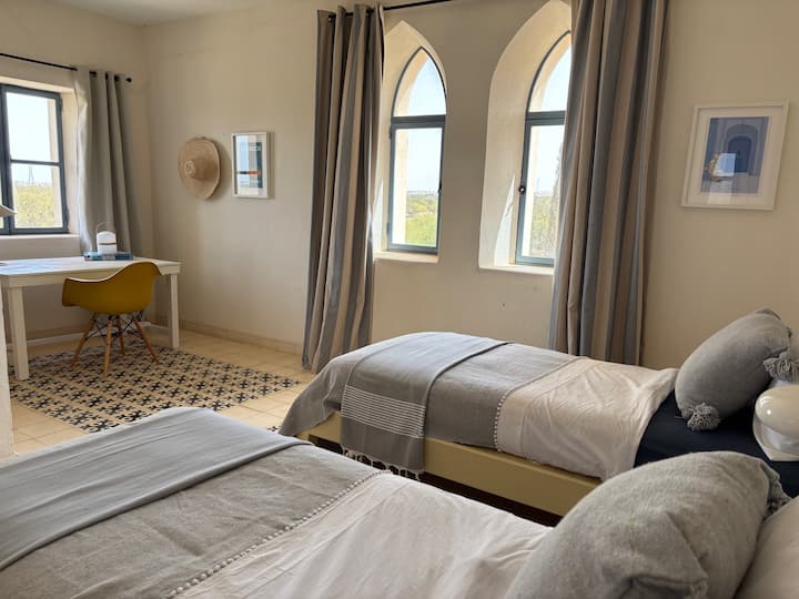 Chambre lumineuse avec lits jumeaux et élégantes fenêtres en arche offrant une belle vue. Décoration douce et épurée, ambiance calme et chaleureuse, idéale pour un séjour reposant en toute sérénité.
