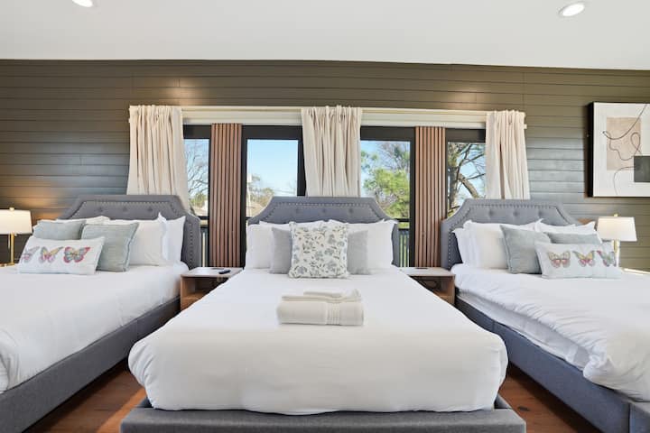 Large Bedroom 5 with three full beds, custom wood accent wall, abundant natural light, and 75" Smart TV.
