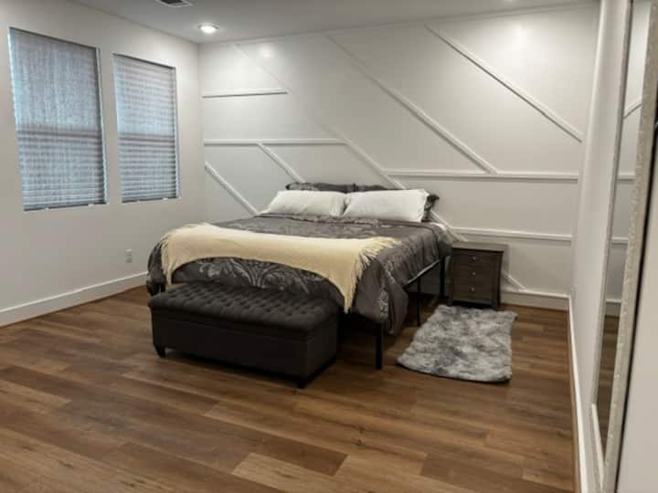 Relax in the spacious primary suite featuring a plush king bed, smart TV, and dedicated workspace with an ergonomic chair. Perfect for workcations, extended stays, or unwinding after a day exploring Houston.