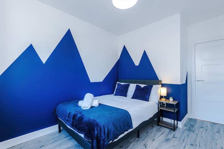Dormitorio luminoso y elegante con una cómoda cama doble, iluminación suave y paredes en azul intenso para crear un ambiente moderno y relajante.