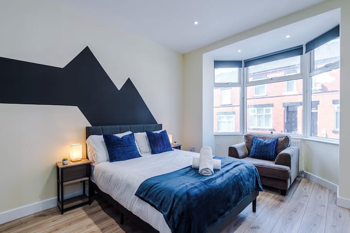 Dormitorio elegante y espacioso con una cómoda cama doble, asientos acogedores y un gran ventanal que deja entrar mucha luz natural.