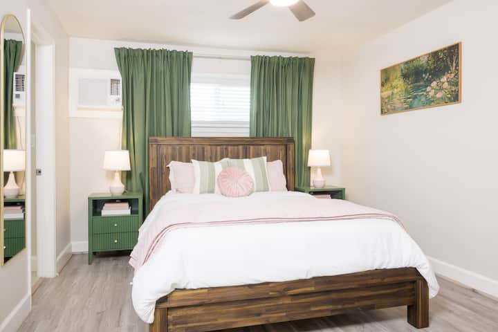 Relax in this serene bedroom featuring a warm wood bed frame, soft pastel bedding, and elegant green accents.