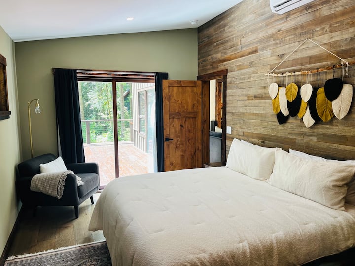 Amplia habitación principal en la planta baja con cama tamaño king, acceso a la terraza, paredes con paneles de madera reciclada y baño privado