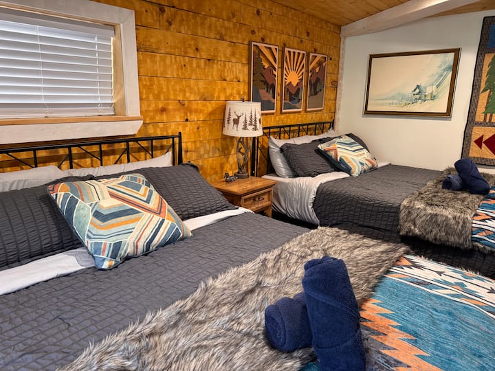 The master bedroom features 2 comfortable queen beds dressed in warm Southwestern-style bedding — cozy, colorful, and perfectly suited to the mountain setting. Wood-paneled walls add rustic character throughout.