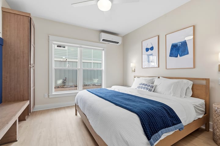 Dormitorio costero con cama tamaño king, ventilador de techo, aire acondicionado y arte con temática de playa