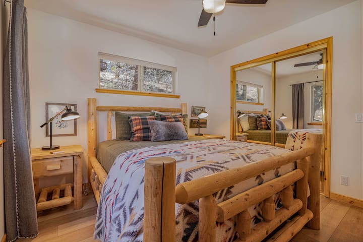 Bedroom 2 offers a comfortable queen bed, warm mountain-style decor, mirrored closet, and natural light — a relaxing space for guests to recharge after a day in Big Bear.