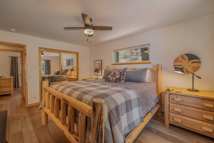 The primary bedroom features a cal king-size log bed, rustic pine furniture, and pine tree views. Private en-suite bath and mirrored closet — your own quiet corner of the mountain.