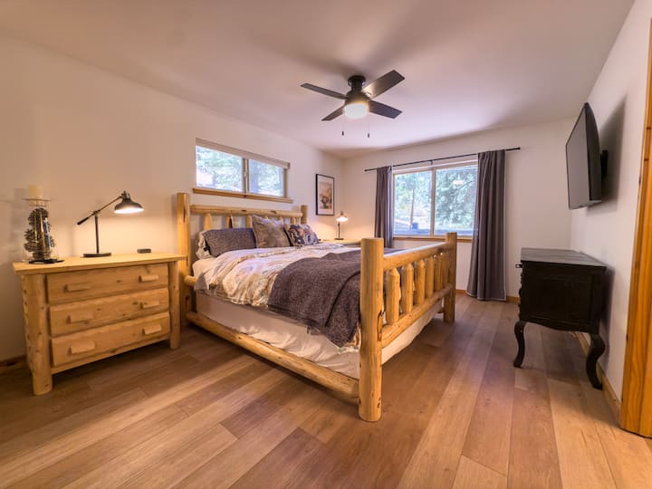 The primary bedroom features a cal king-size log bed, rustic pine furniture, and pine tree views. Private en-suite bath and mirrored closet — your own quiet corner of the mountain.