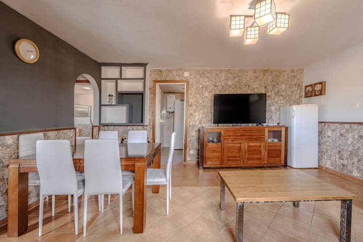Comedor con sillas blancas y TV sobre mueble de madera.