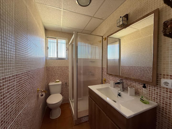 Baño completo con ducha, espejo grande y lavabo.