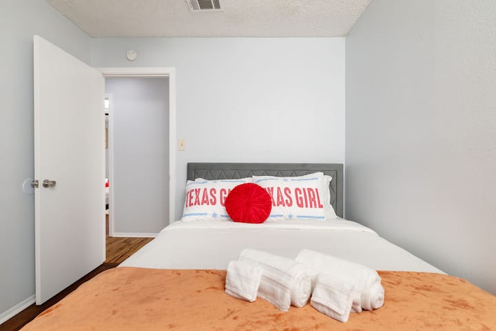 This inviting second bedroom features a queen bed with playful "Texas Girl" pillows and a warm orange throw.