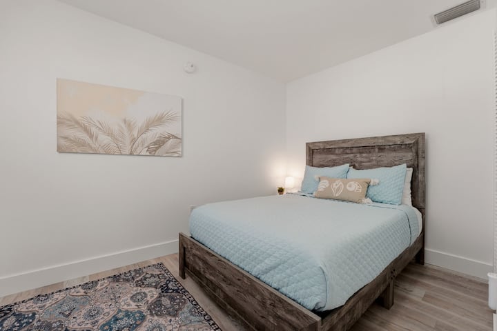 Tercer dormitorio con tonos relajantes y cama de tamaño completo. Una ventana da al patio trasero. La mesita de noche con lámpara, puertos de carga y un despertador con máquina de sonido permite tener todo al alcance de la mano para disfrutar de noches cómodas y tranquilas.