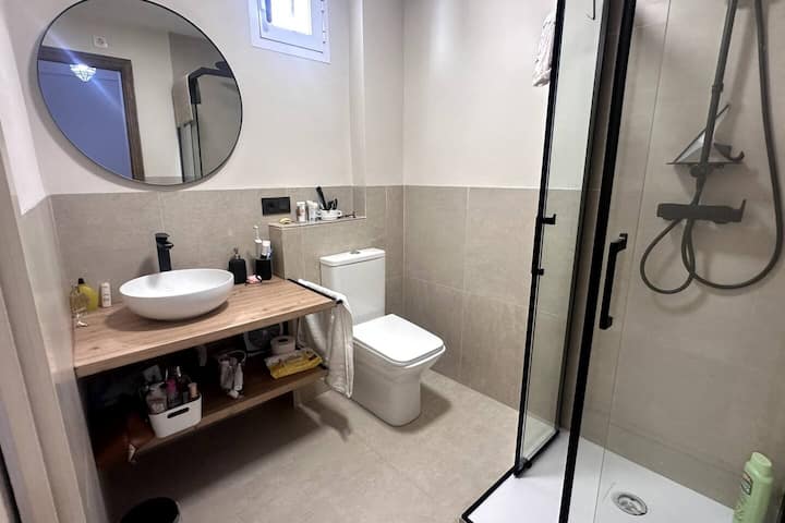 Lavabo sobre encimera de madera, espejo redondo y grifería negra: baño a estrenar