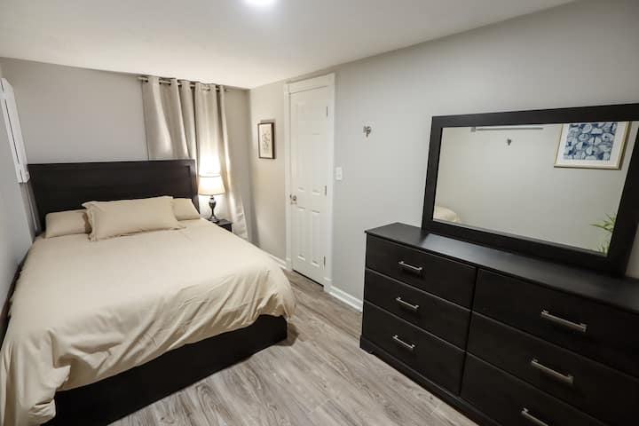 Cama cómoda de tamaño completo, muebles de madera oscura y un espejo grande. Las paredes en gris suave y los tonos neutros crean un ambiente limpio y tranquilo para los huéspedes.  Ubicado en el nivel inferior.