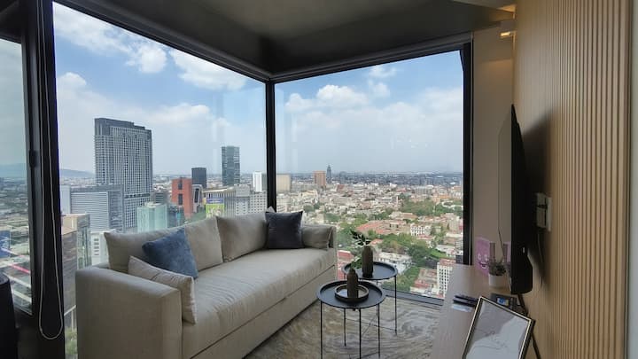 Sala con ventanales de piso a techo y vista panorámica a la Ciudad de México, ideal para disfrutar una experiencia premium en Reforma.