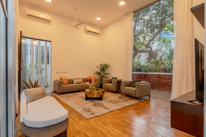 A spacious, sunlit living room with tall glass windows and sheer curtains allowing soft daylight to fill the space.