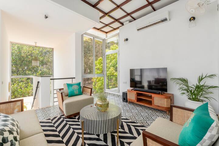 Floor-to-ceiling windows with sheer curtains allow soft daylight to filter in, brightening the entire space. The flooring features intricate patterned tiles that contrast beautifully with the neutral furniture.