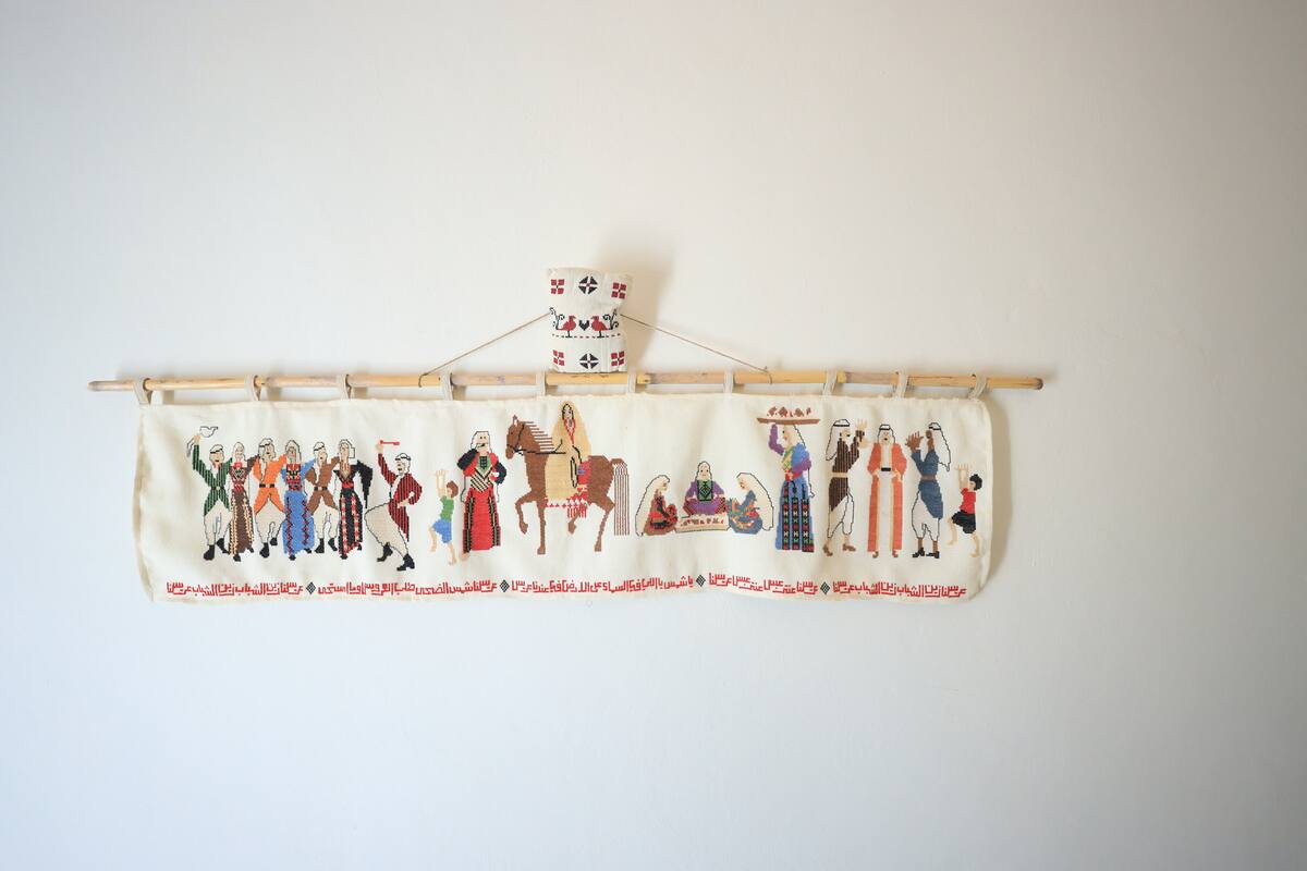 A long embroidered panel of village figures on a white wall