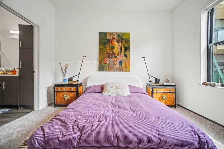 Serene bedroom featuring a plush bed with soft linens, warm wood nightstands, and artistic accents. A calming space designed for restful nights and relaxed mornings.