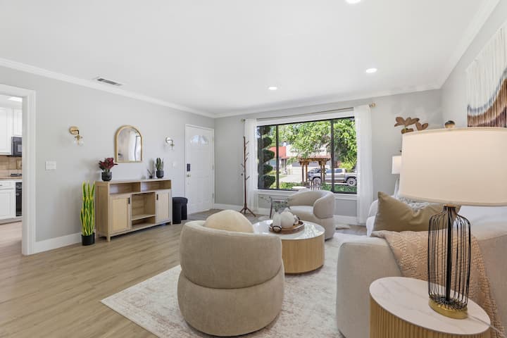 Sunlit living room with large window, chic seating, and warm wood floors