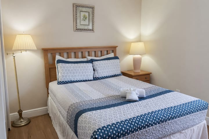 Tranquila recámara con cama king, elegante ropa de cama azul y blanca, dos burós con lámparas y un ambiente cálido y relajante.