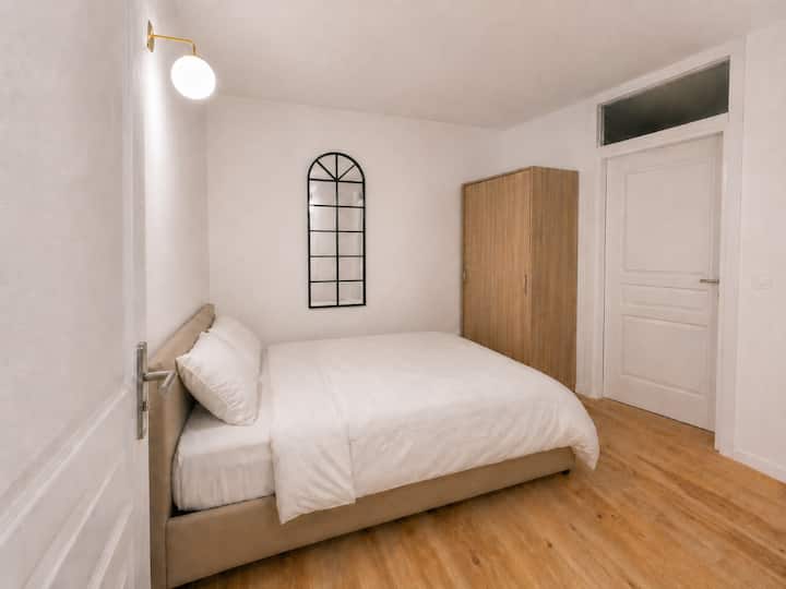 Chambre 2 cosy avec lit double, miroir décoratif arché et armoire. Linge de lit haut de gamme, parquet bois et stores occultants pour des nuits paisibles dans cette pièce intime au cœur de l'appartement.