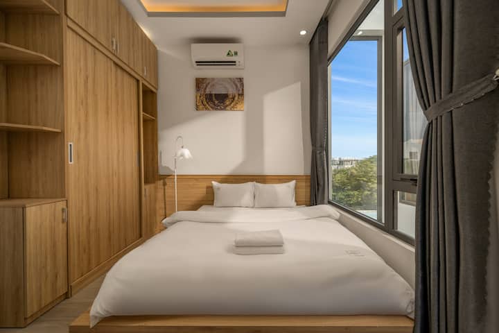Un dormitorio de estilo minimalista con una cama doble de color blanco nítido y una elegante cabecera de madera. El gran sistema de puertas de vidrio ofrece vistas abiertas, combinadas con pinturas artísticas en las paredes y lámparas de pie modernas para crear un espacio de descanso acogedor y lleno de luz.