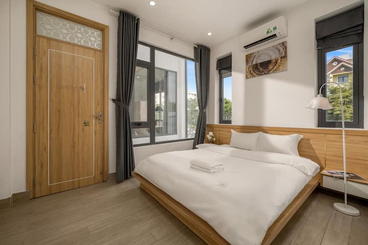 
Elegante dormitorio con una cama doble de color blanco inmaculado sobre un cálido piso de madera. El gran sistema de ventanas con cortinas de color gris oscuro crea una sensación de amplitud y profundidad en el espacio. Los muebles de madera de color claro consistentes, desde la puerta hasta la cabecera, combinados con elegantes lámparas de pie, crean una sensación de tranquilidad.