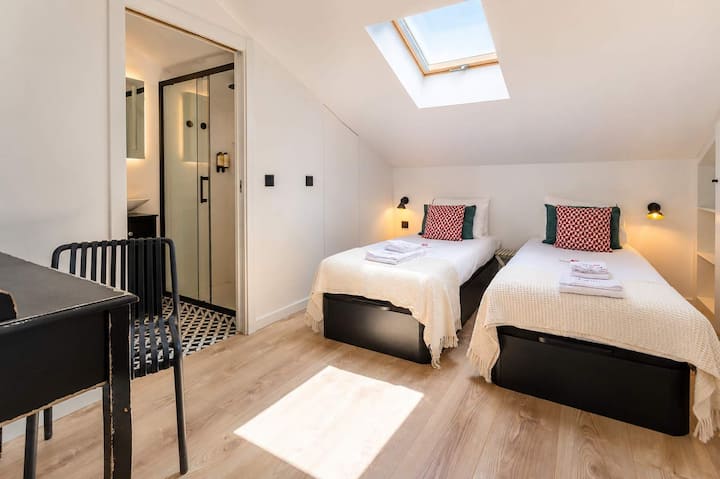 20 · Dormitorio con camas individuales, tragaluz y puerta al baño privado · StayInLisbon