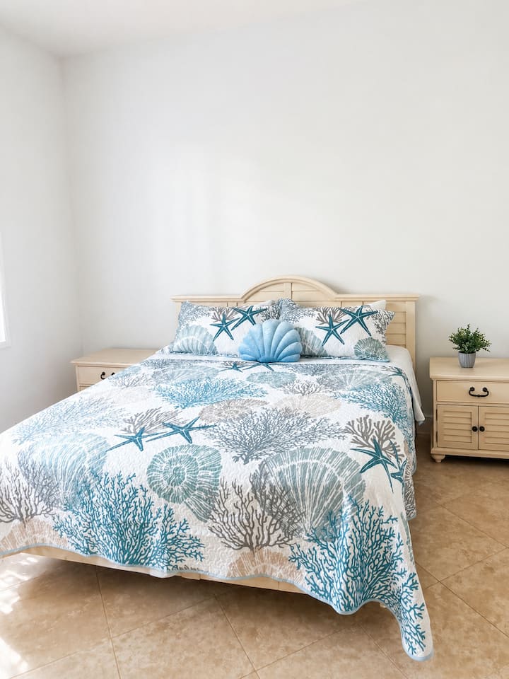 Relaxing king bedroom with beach-inspired bedding, soft coastal colors, and a clean, comfortable layout for a restful island getaway.