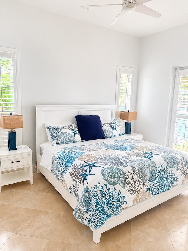 Coastal king bedroom with bright natural light, beach-inspired decor, nightstands, and peaceful private island style.