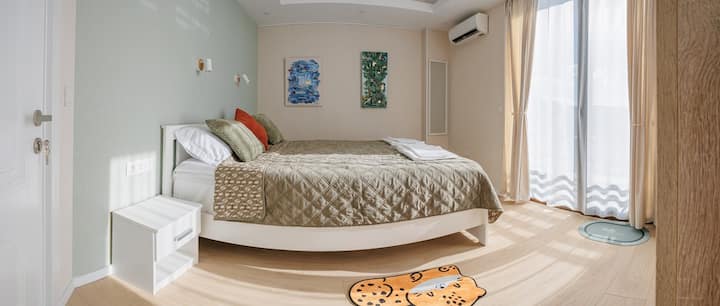 Separate bedroom with a queen-size bed, air conditioning, blackout curtains, and original artwork by Inessa Gogia.
