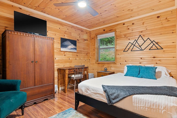 Acogedora recámara con paneles de madera, cama tamaño queen, escritorio, TV y vistas serenas a la naturaleza