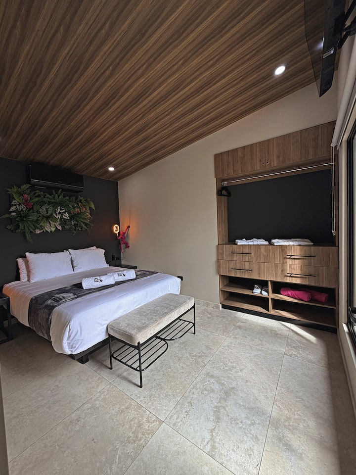 Habitación secundaria con cama queen, ropa de cama de calidad hotelera, aire acondicionado, TV, amplio espacio de almacenamiento y banca tipo otomana para una estadía cómoda.
