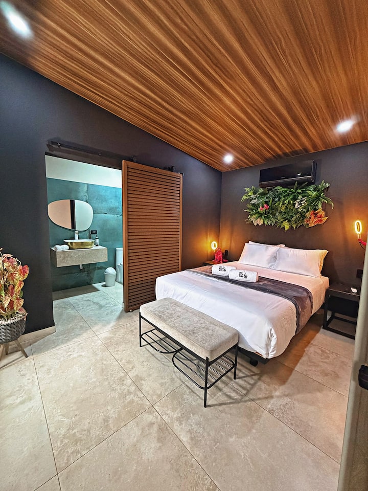 Habitación principal con cama queen, baño privado, aire acondicionado, detalles decorativos tropicales y banca tipo otomana para mayor comodidad durante la estadía.