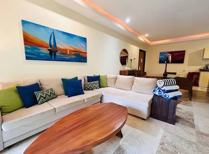 Détendez-vous sur ce grand canapé modulaire en forme de « L », agrémenté de divers coussins décoratifs qui ajoutent des touches de bleu marine et de vert émeraude, ou passez un après-midi convivial en famille ou entre amis.