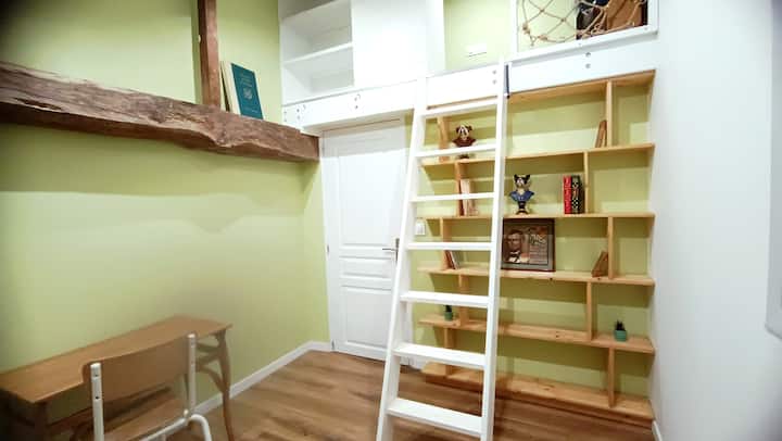 Una habitación estilo cabaña, con una zona de escritorio y una zona de descanso con una cama individual que parece suspendida en un nido íntimo.