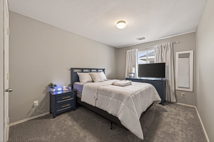 El cuarto dormitorio cuenta con un televisor de 43", una lámpara Alexa, un cargador inalámbrico 3 en 1, un espejo de cuerpo entero, cortinas opacas, una cómoda y una cama tamaño queen. 