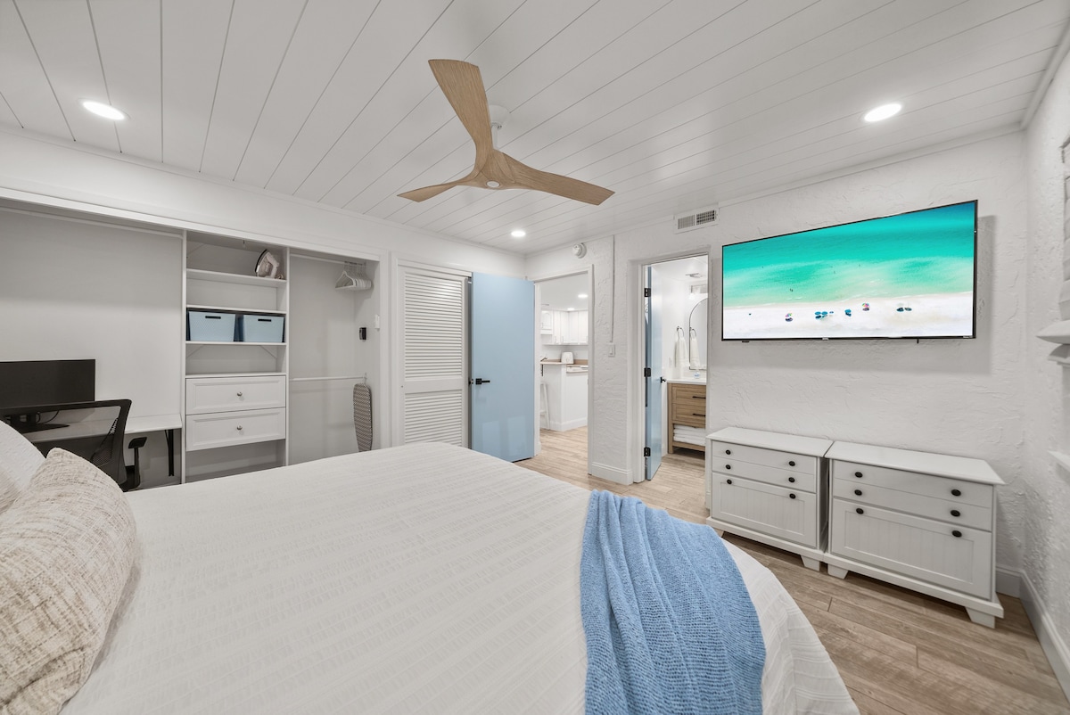 Primary bedroom with smart tv and desk/workstation area with an extra computer monitor. Shiplap ceiling with fan and dimmable lights. King size bed