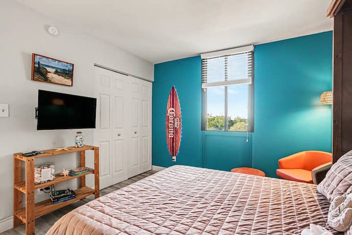 CAMA QUEEN Cama abatible Paredes verde azulado, ropa de cama de un naranja vibrante y una tabla de surf de verdad. Divertido, alegre y lleno de energía playera.