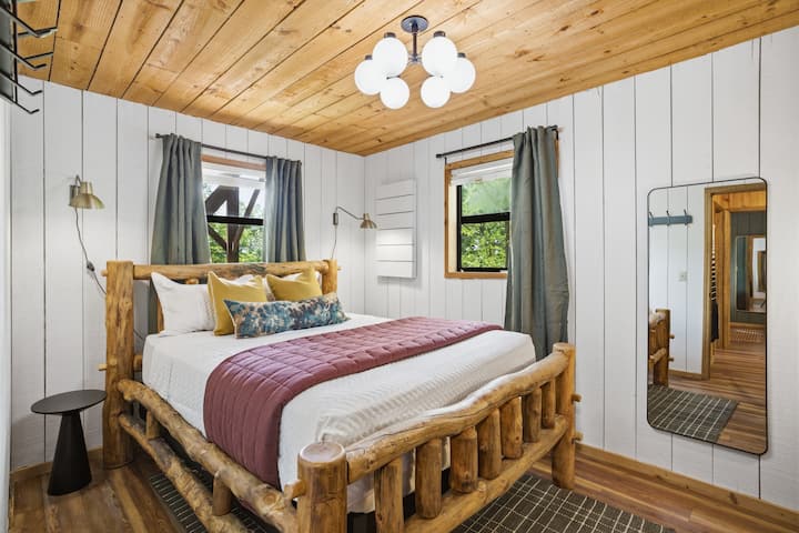 Dormitorio en la planta baja cuidadosamente diseñado con un acabado blanco y un ambiente tranquilo. Incluye una cama tamaño queen en la que duermen dos personas cómodamente, junto con un espacio de trabajo privado para trabajar a distancia o planificar tus aventuras en Smoky Mountain.