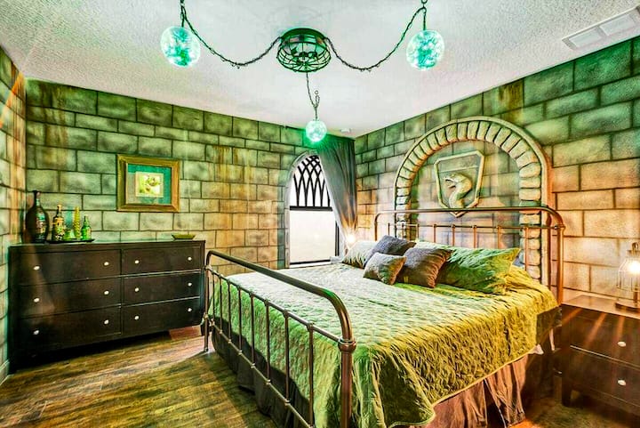 Green dungeon light, stone walls, a serpent crest glowing above the iron-frame bed — the Emerald Serpent Suite runs deeper than the others. Slytherin always does.