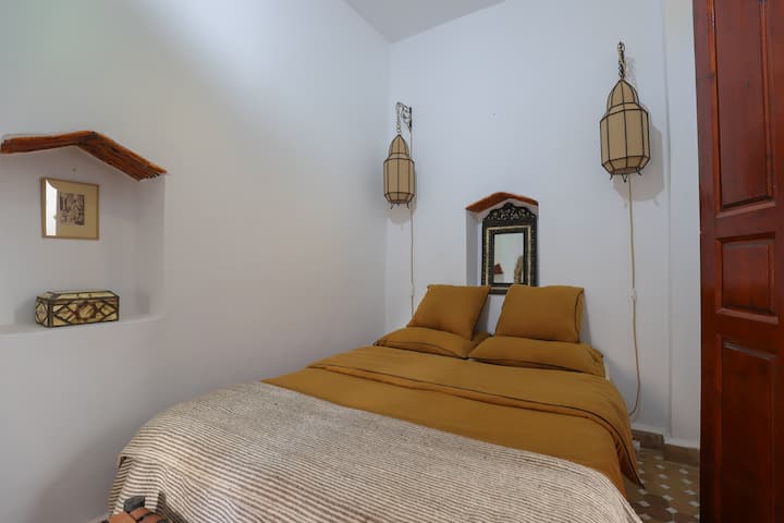Chambre cosy au style marocain épuré avec literie confortable, lanternes artisanales et ambiance douce propice au repos.