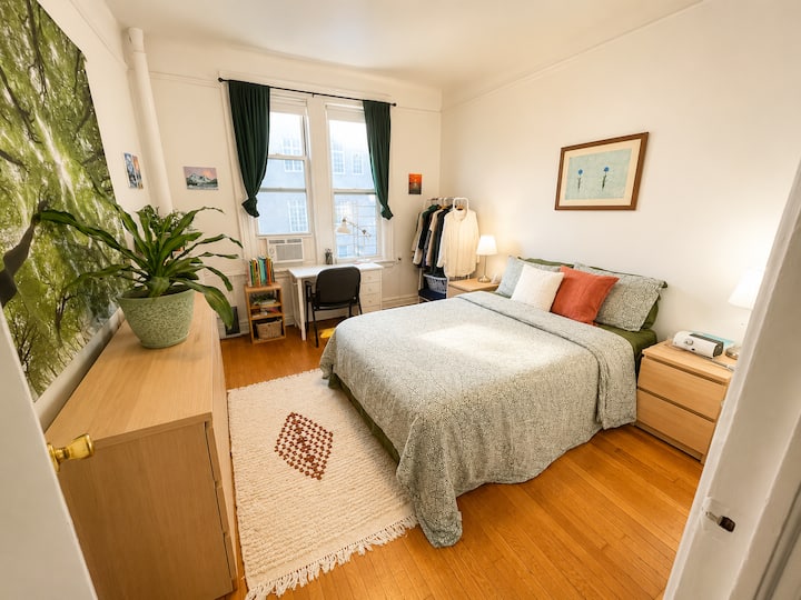 Recámara luminosa y tranquila con una cómoda cama tamaño queen, cortinas opacas, pisos de madera y una cálida luz natural durante todo el día.