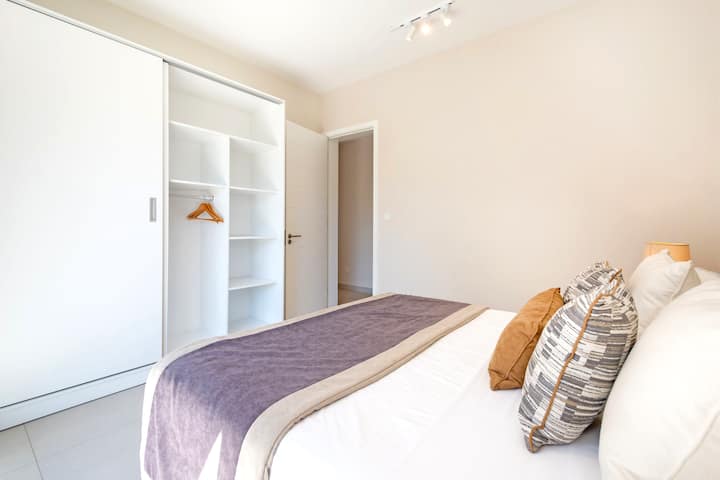 Chambre avec lit queen size, literie soignée et grand dressing intégré avec penderie et étagères. Décor neutre et épuré, ambiance calme et reposante.
