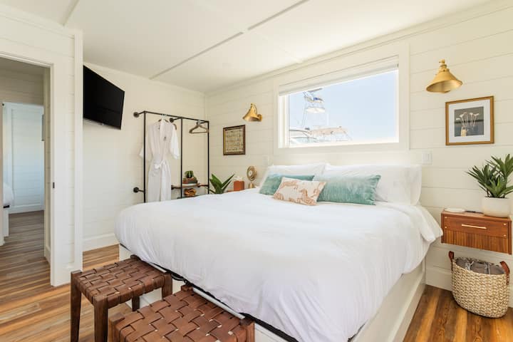 Una suite principal privada con cama tamaño king, paredes de tablas superpuestas, apliques de latón, vista a la marina desde la ventana, batas de cortesía y un baño privado dedicado justo al otro lado de la puerta.
