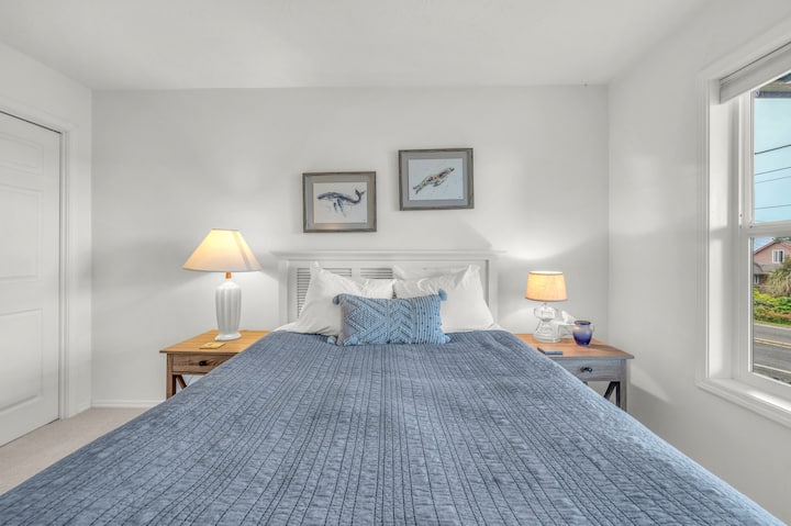 Tu tranquila habitación costera te espera con sábanas suaves, una cálida iluminación junto a la cama y encantadoras obras de arte náuticas, perfecta para noches de descanso después de explorar la costa.
